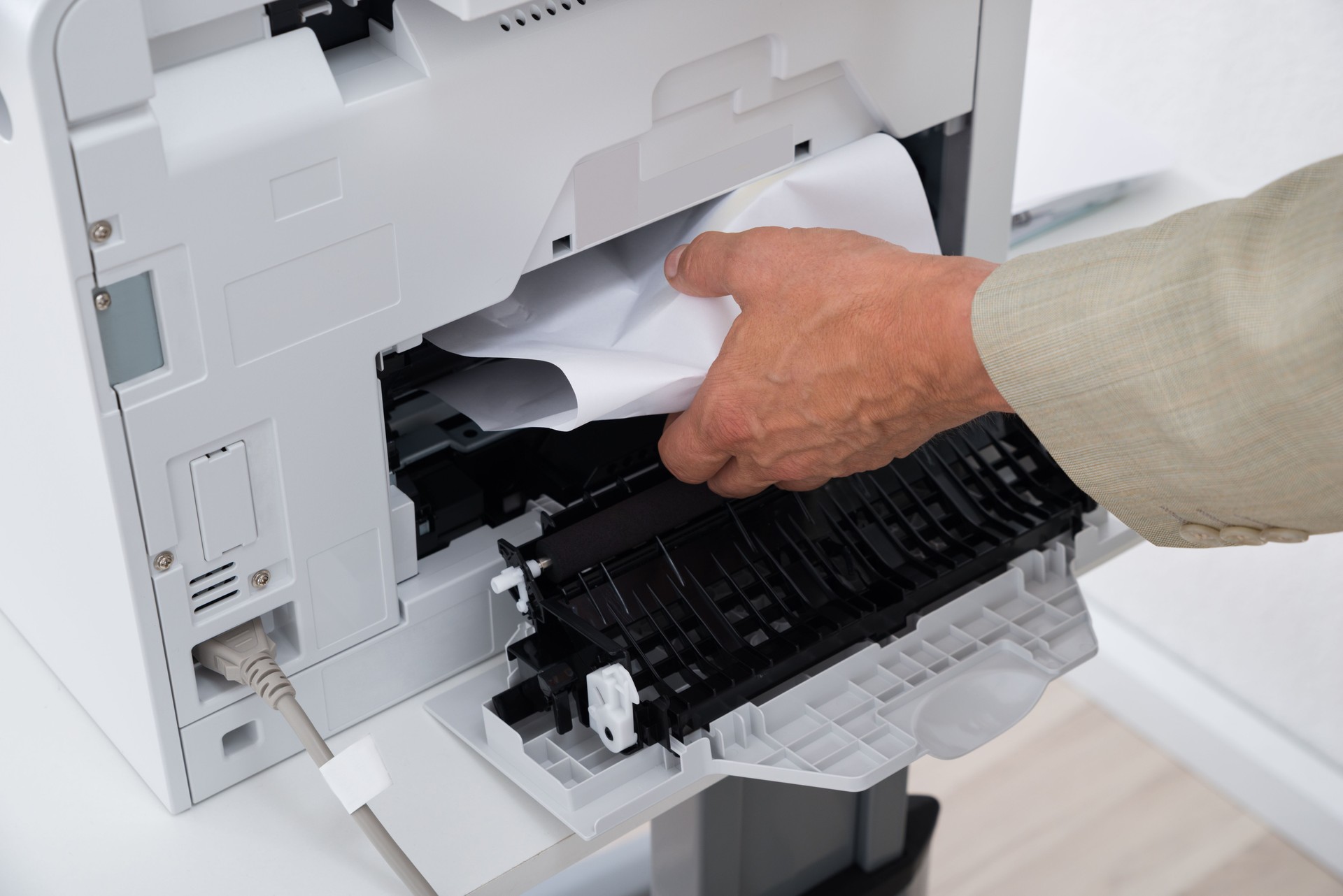 Businessman's Hand Removing Paper Stuck In Printer